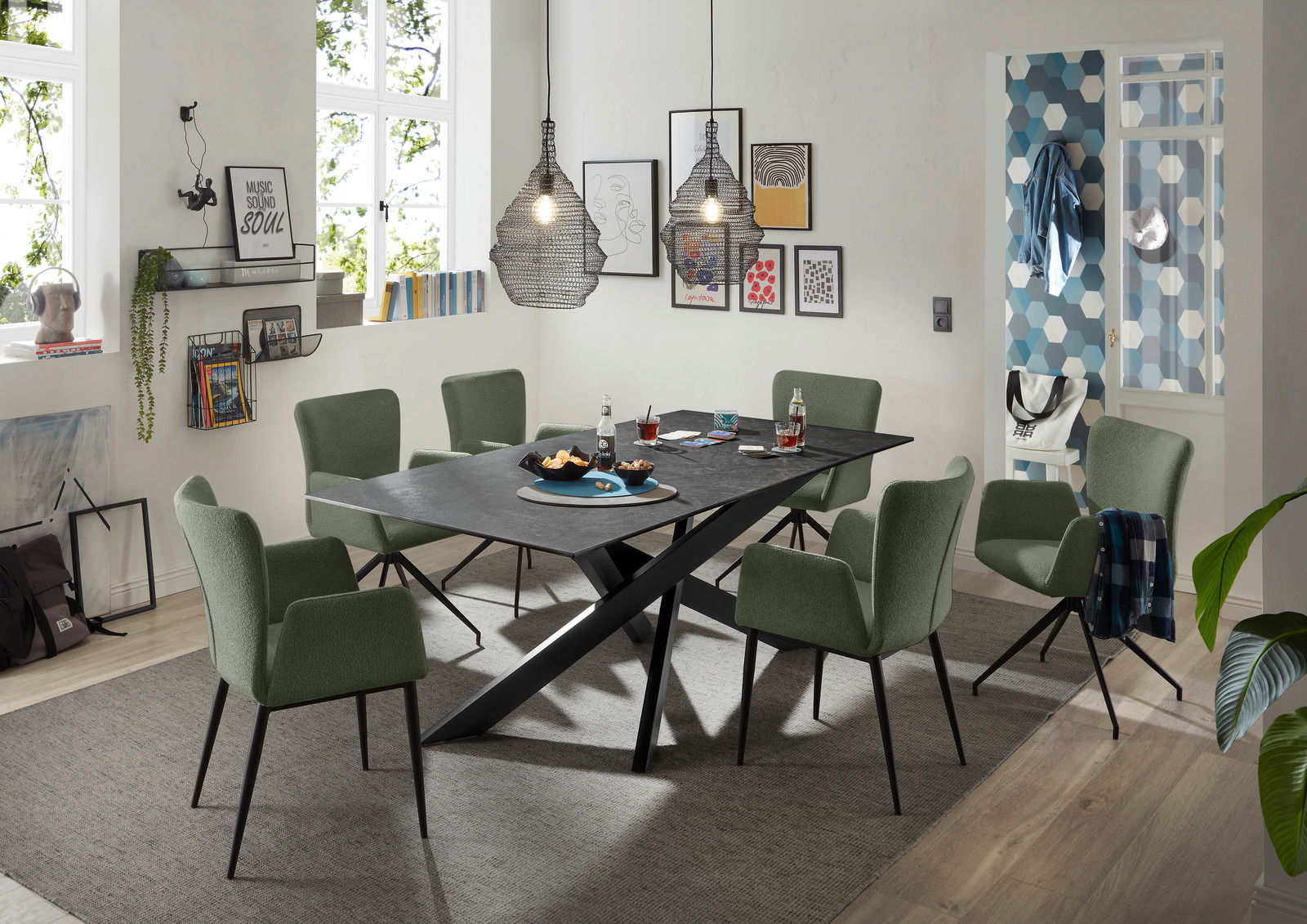 Moderner Esstisch mit schwarzer Tischplatte und X-förmigem Gestell, umgeben von grünen Stühlen in einem stilvoll eingerichteten Esszimmer, seitliche Perspektive.