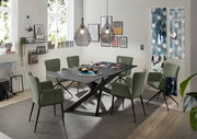 Moderner Esstisch mit schwarzer Tischplatte und X-förmigem Gestell, umgeben von grünen Stühlen in einem stilvoll eingerichteten Esszimmer, seitliche Perspektive.