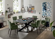 Moderner Esstisch mit schwarzer Tischplatte und X-förmigem Gestell, umgeben von grünen Stühlen in einem stilvoll eingerichteten Esszimmer, seitliche Perspektive.