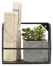 Nahaufnahme eines Wandregals mit einer gerollten Karte und einer kleinen Pflanze in einem Steintopf, seitliche Perspektive.