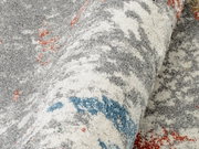 Nahaufnahme eines Frisé-Teppichs mit grauen, weißen, blauen und roten Mustern, gerollt dargestellt.