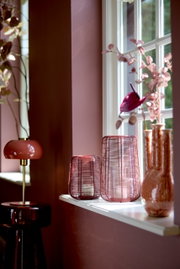 Tischleuchte in elegantem Design mit rotem Schirm und goldfarbenem Ständer, seitliche Perspektive, platziert auf einem dunklen Beistelltisch vor einer rosa Wand.