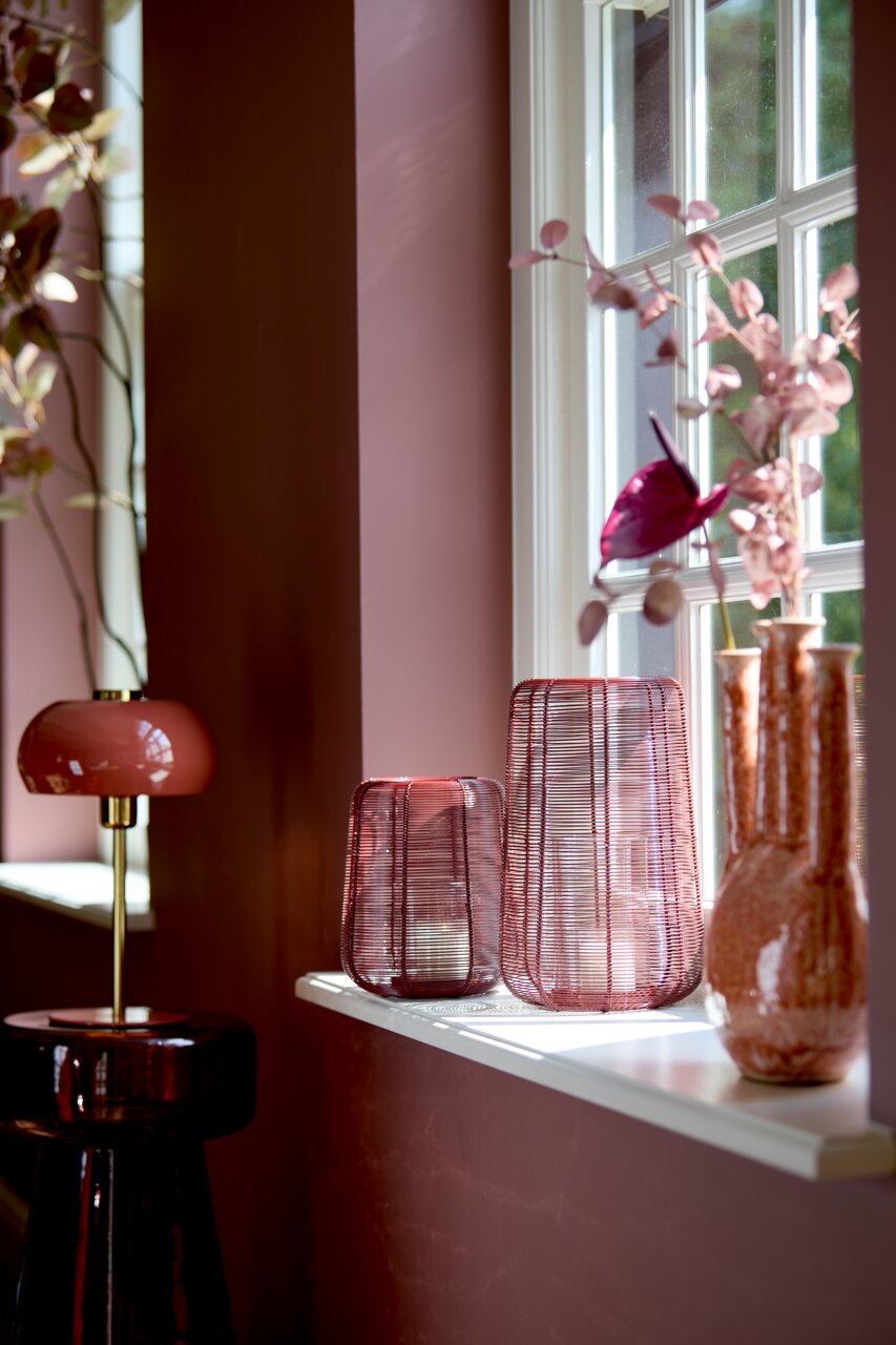 Tischleuchte in elegantem Design mit rotem Schirm und goldfarbenem Ständer, seitliche Perspektive, platziert auf einem dunklen Beistelltisch vor einer rosa Wand.