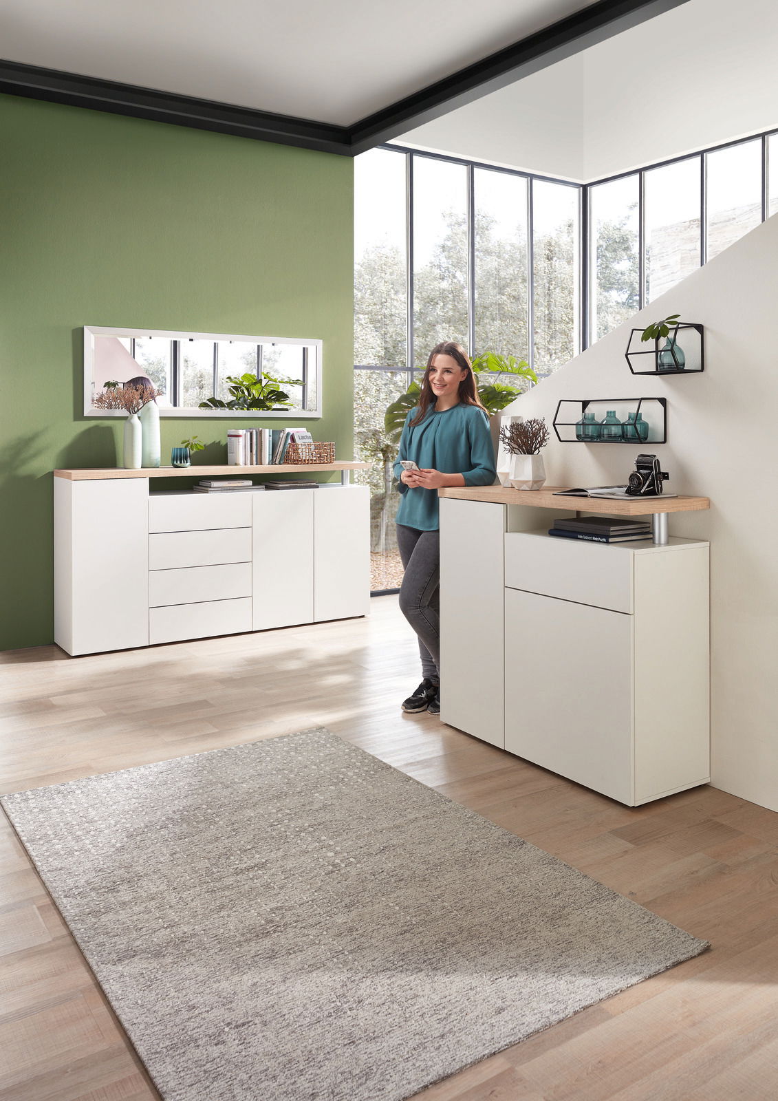 Landscape Wandregal NORA Moderner Wohnraum mit weißem Sideboard und Wandregal, dekoriert mit Pflanzen und Büchern, im Vordergrund eine Frau in entspannter Pose. Perspektive: seitlich von vorne.