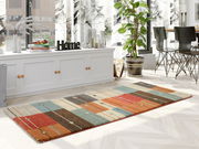 Frisé-Teppich in einem modernen Wohnzimmer, mit buntem geometrischem Muster in Rot, Blau, Braun und Beige, auf hellem Holzboden vor einem Fenster mit Pflanzen und Dekorationen. Perspektive von schräg oben.