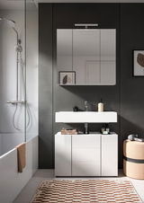 Moderner Waschbeckenunterschrank VIRA in einem stilvollen Badezimmer, frontal betrachtet. Der Schrank ist weiß und bietet Stauraum unter einem rechteckigen Waschbecken. Darüber befindet sich ein großer Spiegel. Die Umgebung ist elegant mit einer Dusche un