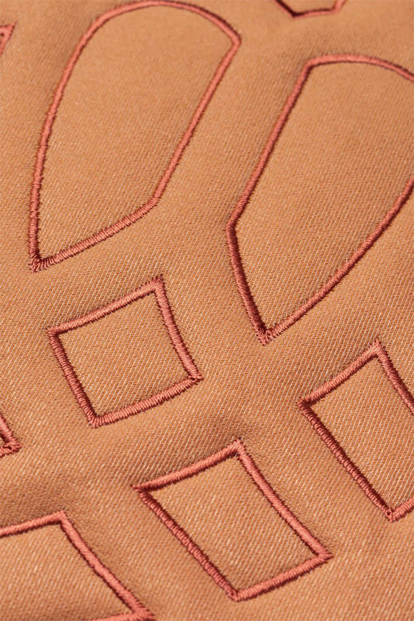 Nahaufnahme einer Zierkissenhülle mit geometrischen Stickmustern in warmen Brauntönen.