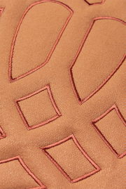 Nahaufnahme einer Zierkissenhülle mit geometrischen Stickmustern in warmen Brauntönen.