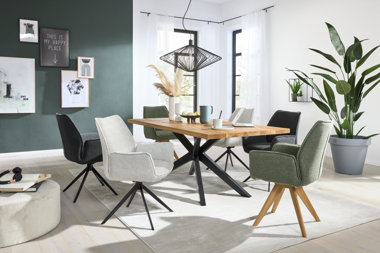 Esszimmer mit modernem Esstisch aus Holz und mehreren Armlehnstühlen in verschiedenen Farben, seitliche Perspektive.