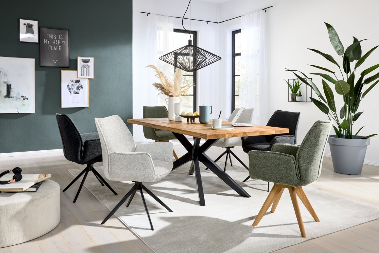 Eetkamer met een moderne houten eettafel en verschillende stoelen met armleuningen in diverse kleuren, zijaanzicht.