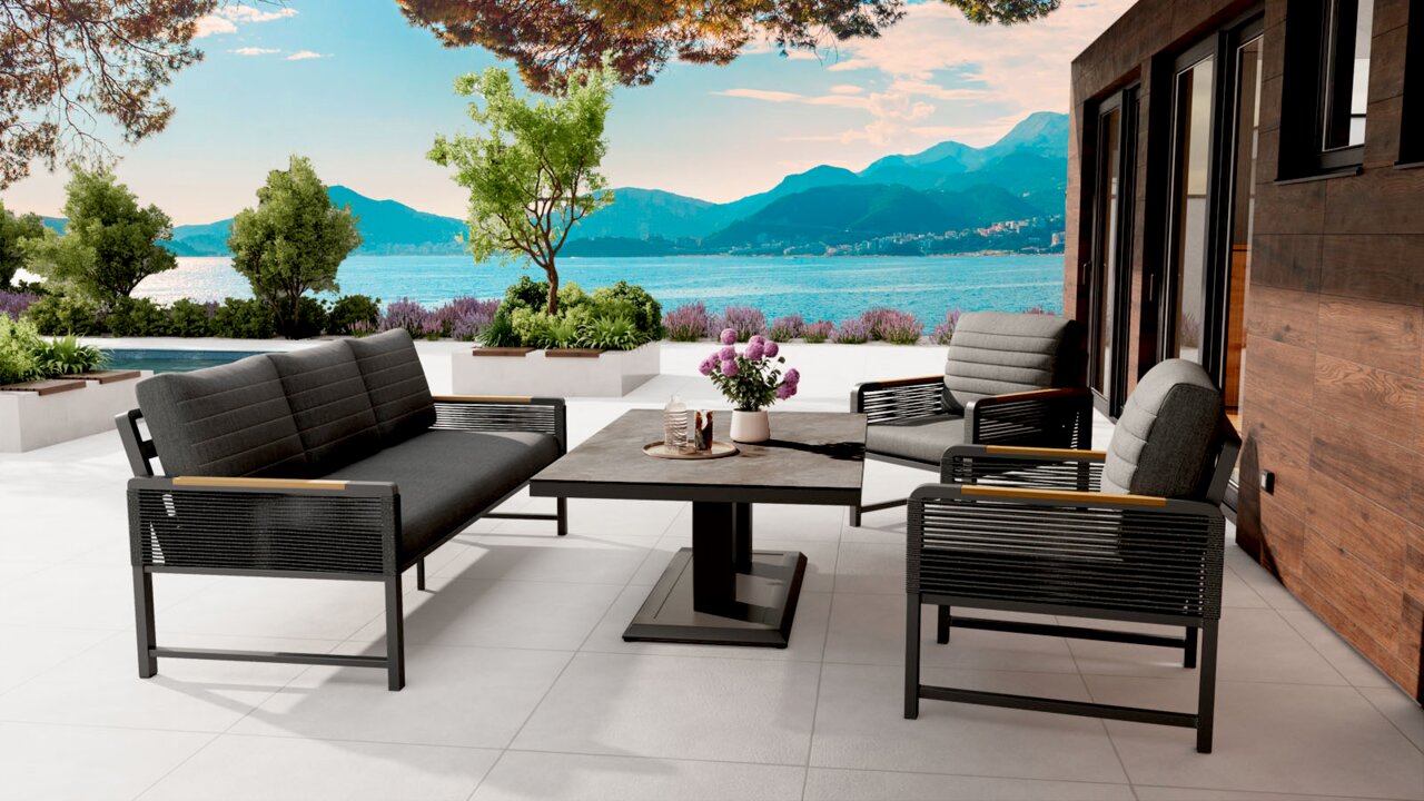 Ambia Garden Sitzbank 3-sitzig CALIDA Moderne Outdoor-Loungegruppe mit grauem 2-Sitzer-Sofa, zwei Sesseln und rechteckigem Couchtisch auf einer Terrasse am See, Perspektive: leicht seitliche Vorderansicht