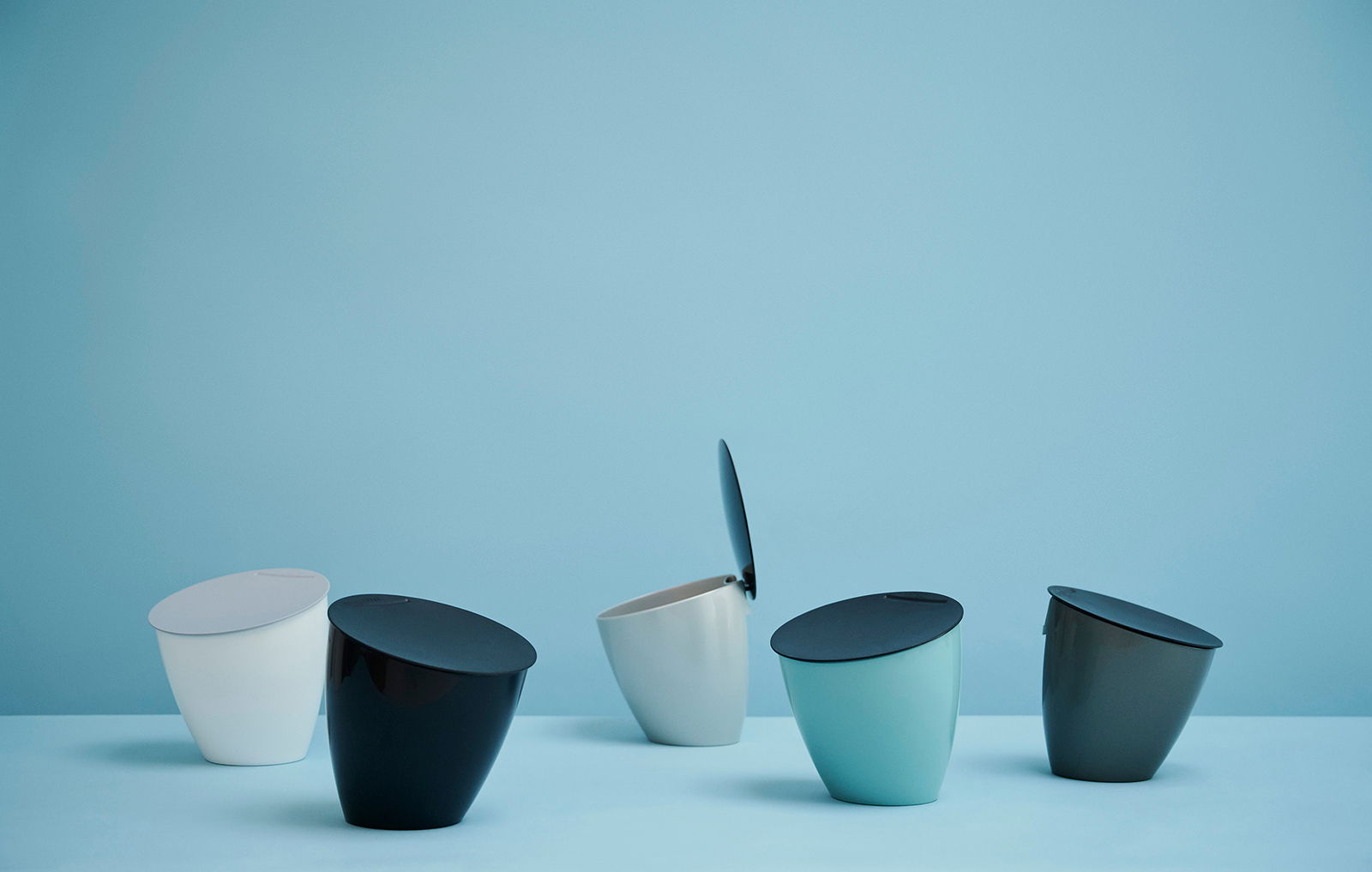 Fünf Bio-Abfallbehälter in verschiedenen Farben, schräg von der Seite fotografiert, auf einem blauen Hintergrund.