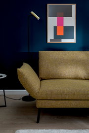 Gelbes Longchair-Sofa in modernem Wohnzimmer, seitliche Perspektive mit Stehlampe und abstraktem Kunstwerk an der Wand.
