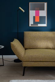 Gelbes Longchair-Sofa in modernem Wohnzimmer, seitliche Perspektive mit Stehlampe und abstraktem Kunstwerk an der Wand.