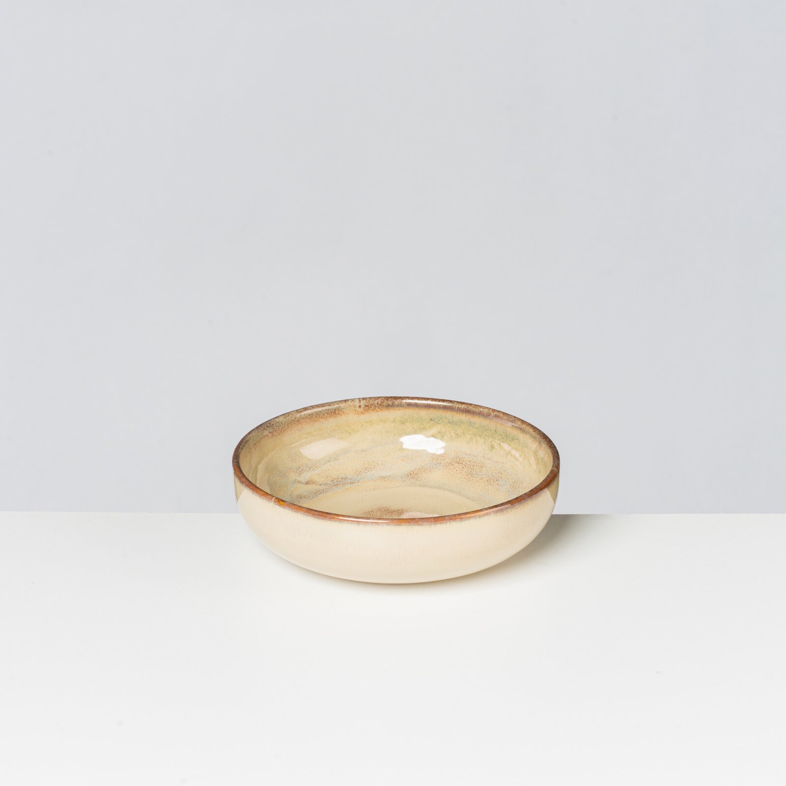 Runde Keramikschale in Creme mit braunem Rand und gesprenkelter Glasur, freigestellt vor hellem Hintergrund, fotografiert in leichter Draufsicht von vorne