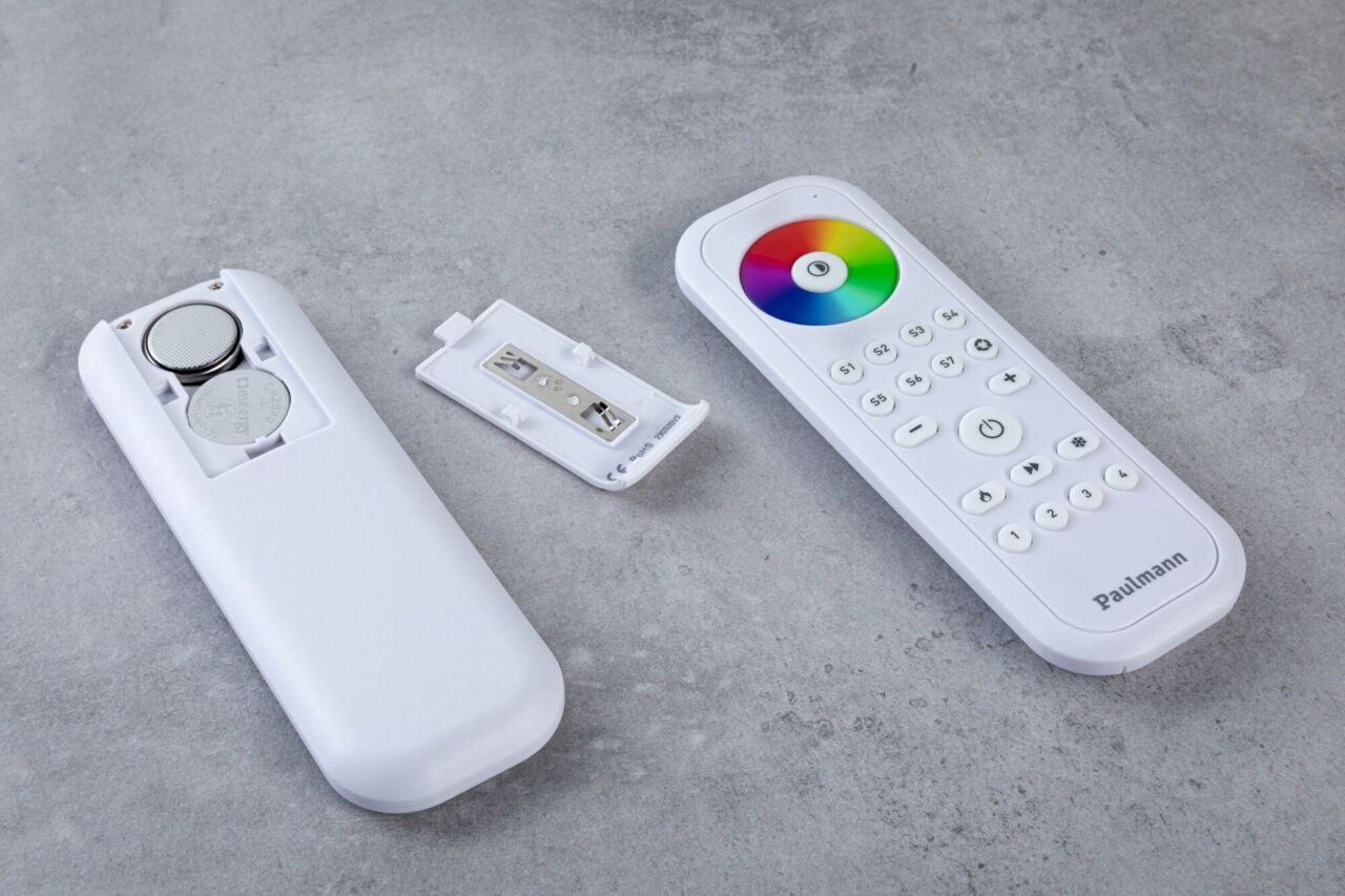 Fernbedienung mit abgenommenem Batteriefachdeckel, zeigt Batterien und bunte Steuerungstasten, von oben betrachtet.