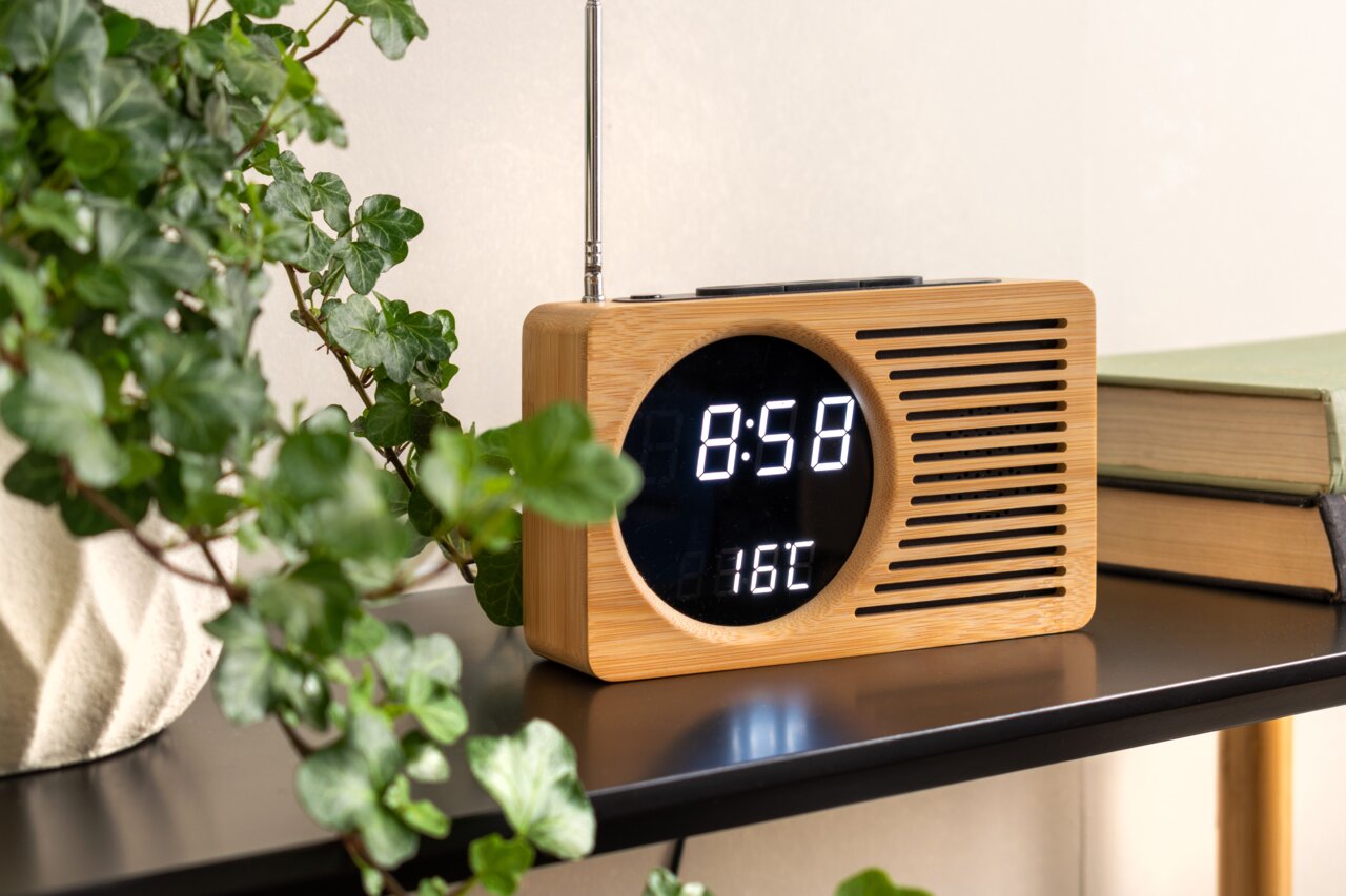 Radiowecker aus Holz mit digitaler Anzeige, umgeben von Pflanzen, seitliche Perspektive