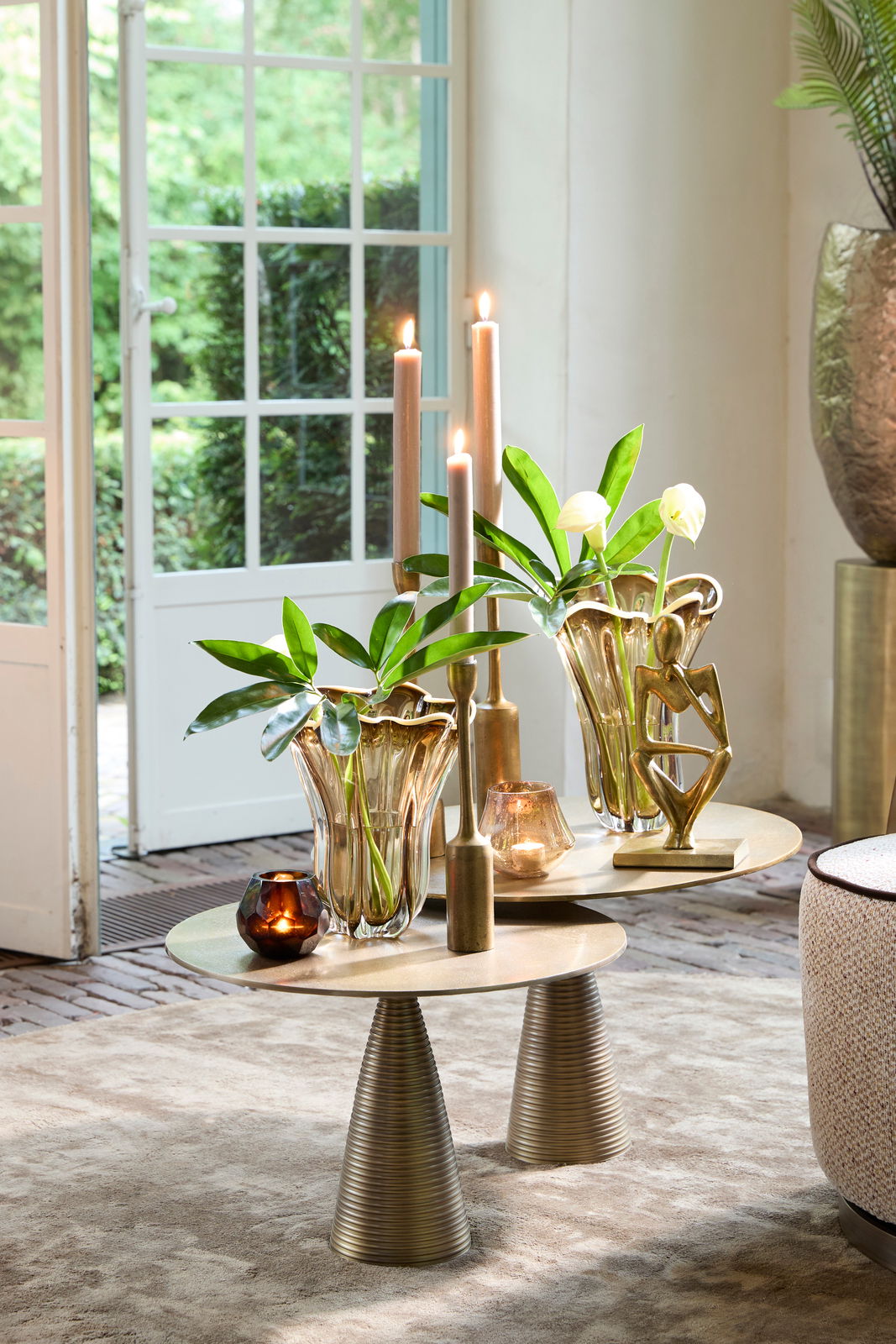 Elegante Vase aus Glas mit wellenförmigem Rand, gefüllt mit grünen Blättern, auf einem modernen Tisch in einem hellen Raum mit Blick auf den Garten.