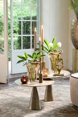 Elegante Vase aus Glas mit wellenförmigem Rand, gefüllt mit grünen Blättern, auf einem modernen Tisch in einem hellen Raum mit Blick auf den Garten.