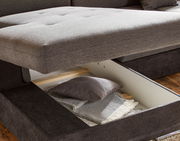 Nahaufnahme einer grauen Rundecke mit geöffneter Stauraumfunktion, die Kissen und Decken zeigt.