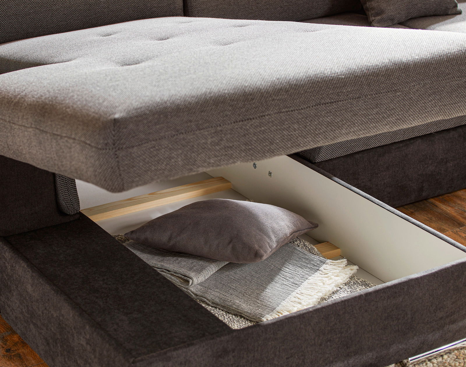 Nahaufnahme einer grauen Rundecke mit geöffneter Stauraumfunktion, die Kissen und Decken zeigt.