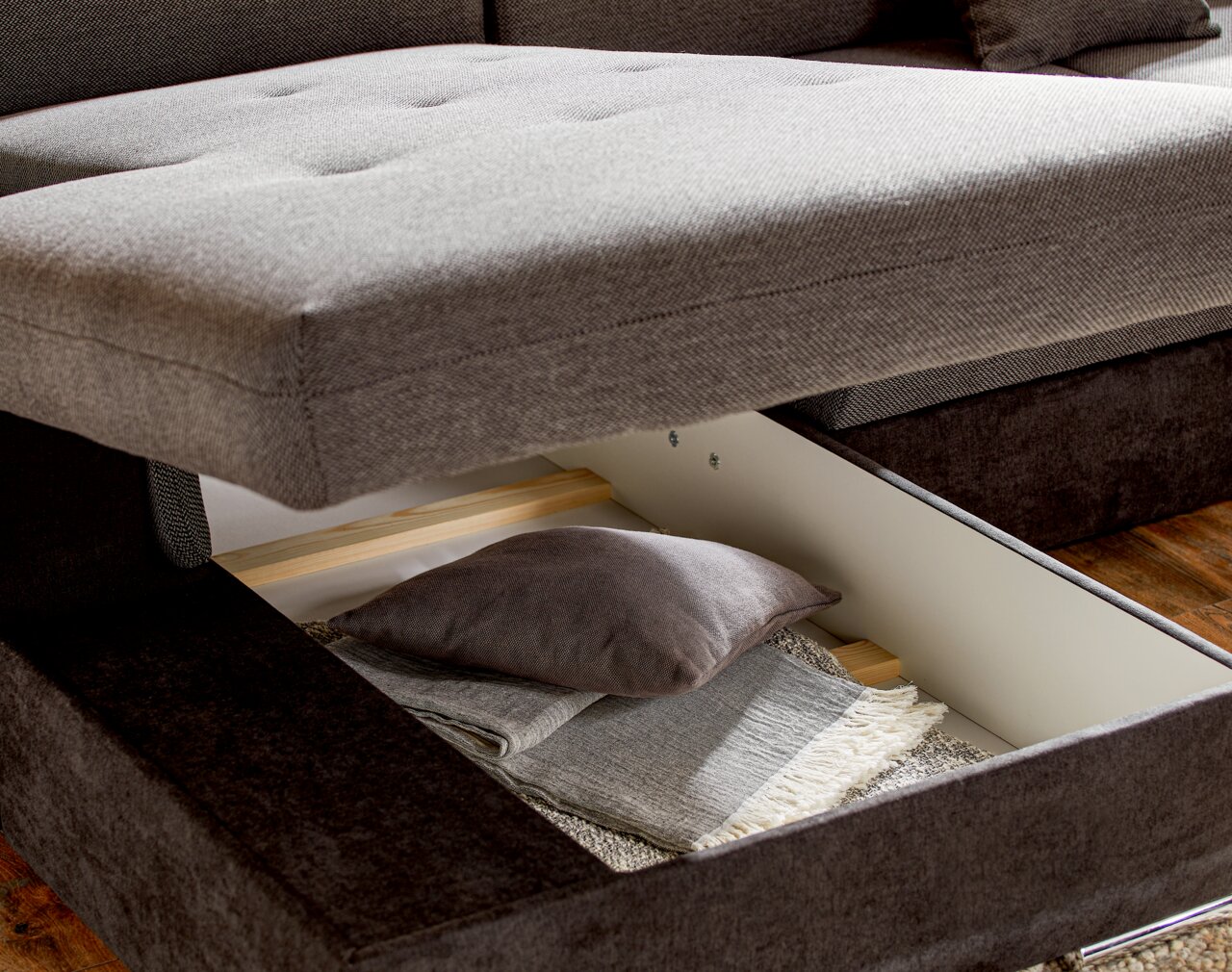 Nahaufnahme einer grauen Rundecke mit geöffneter Stauraumfunktion, die Kissen und Decken zeigt.