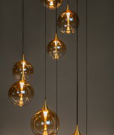 Mehrere hängende Leuchten mit goldenen, kugelförmigen Glasschirmen, die von der Decke hängen. Die Perspektive zeigt die Leuchten von der Seite.
