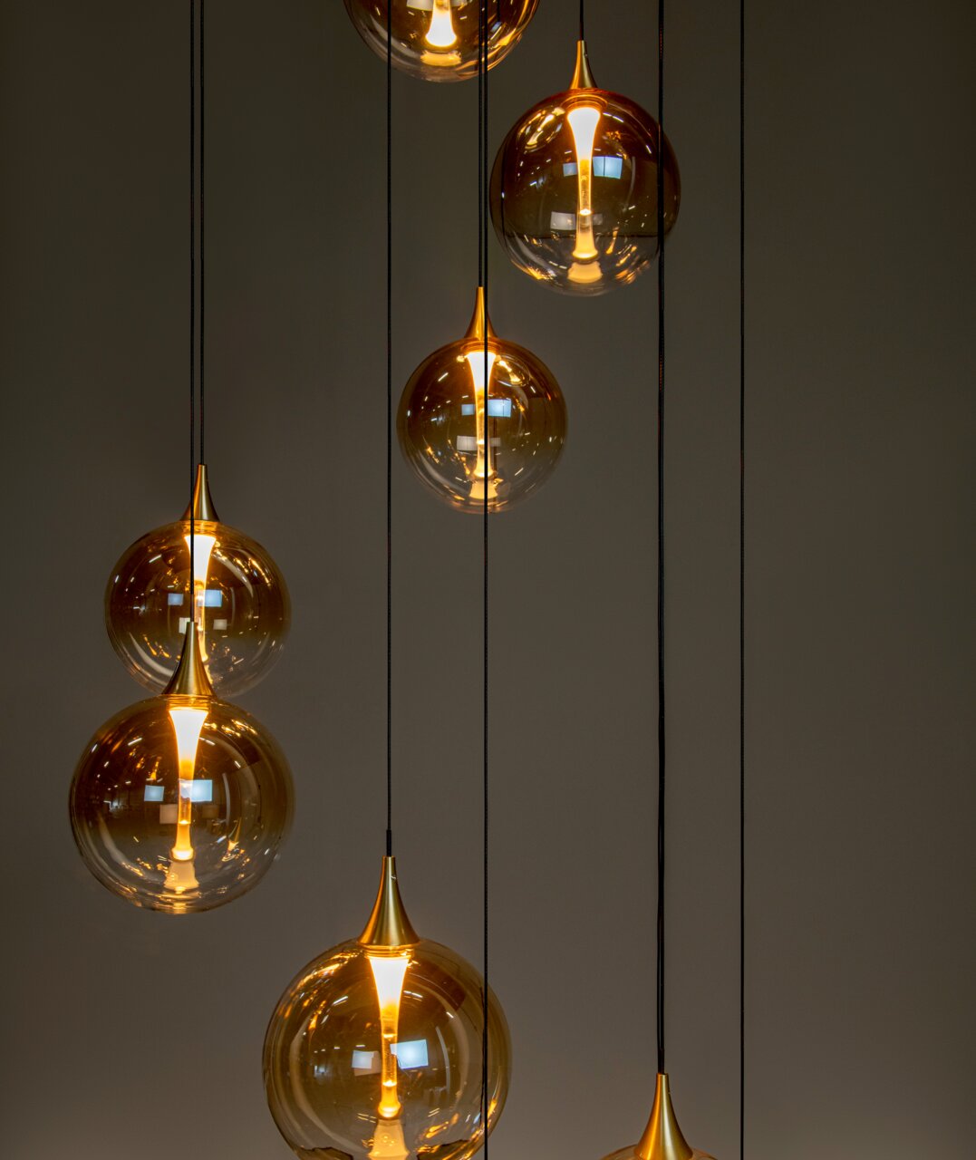 Mehrere hängende Leuchten mit goldenen, kugelförmigen Glasschirmen, die von der Decke hängen. Die Perspektive zeigt die Leuchten von der Seite.