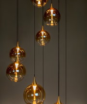 Mehrere hängende Leuchten mit goldenen, kugelförmigen Glasschirmen, die von der Decke hängen. Die Perspektive zeigt die Leuchten von der Seite.