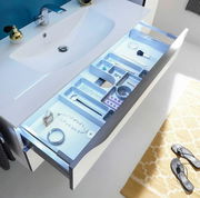 Moderne Badkombination mit Waschbecken und geöffneter Schublade, die von oben gezeigt wird. Die Schublade enthält verschiedene Fächer zur Aufbewahrung von Schmuck und Kosmetikartikeln.