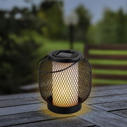 Metalen zonne-lantaarn met gaasmotief, brandend op een houten tafel, zijaanzicht