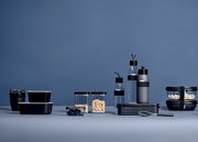 Verschillende zwarte bewaardozen en drinkflessen in een moderne, minimalistische opstelling tegen een blauwe achtergrond, gezien vanuit een zijdelingse hoek.