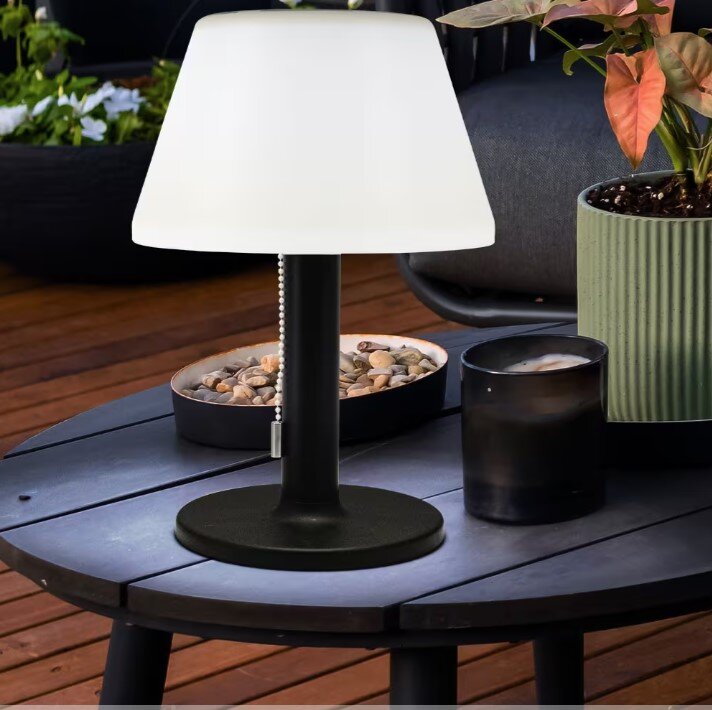 Zonne-tafellamp van 28 cm, zwart, op een houten tafel buiten, omringd door planten en decoraties, zijaanzicht
