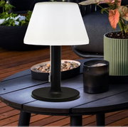 Zonne-tafellamp van 28 cm, zwart, op een houten tafel buiten, omringd door planten en decoraties, zijaanzicht