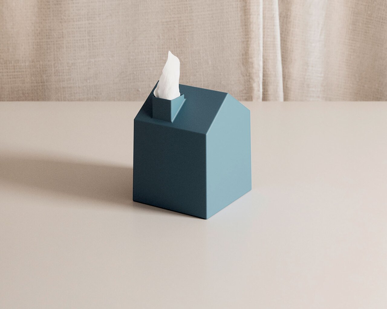 Petrolfarbene Kosmetiktuchbox in moderner Hausform mit herausragendem weißem Tuch, aus leicht erhöhter Vorderansicht auf einem hellen Tisch präsentiert