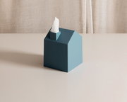 Petrolfarbene Kosmetiktuchbox in moderner Hausform mit herausragendem weißem Tuch, aus leicht erhöhter Vorderansicht auf einem hellen Tisch präsentiert