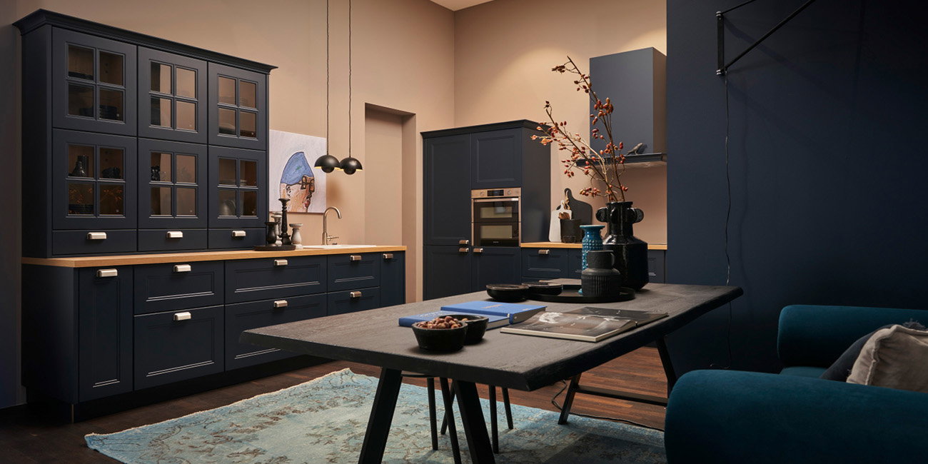 Die Küche hat dunkelblaue Schränke mit Glasfronten und eine helle Holz-Arbeitsplatte.