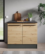 Frontansicht eines modernen Spülenunterschranks aus Holz mit dunkler Arbeitsplatte, dekoriert mit Schneidebrett, Öl- und Essigflaschen sowie einem Kräutertopf.