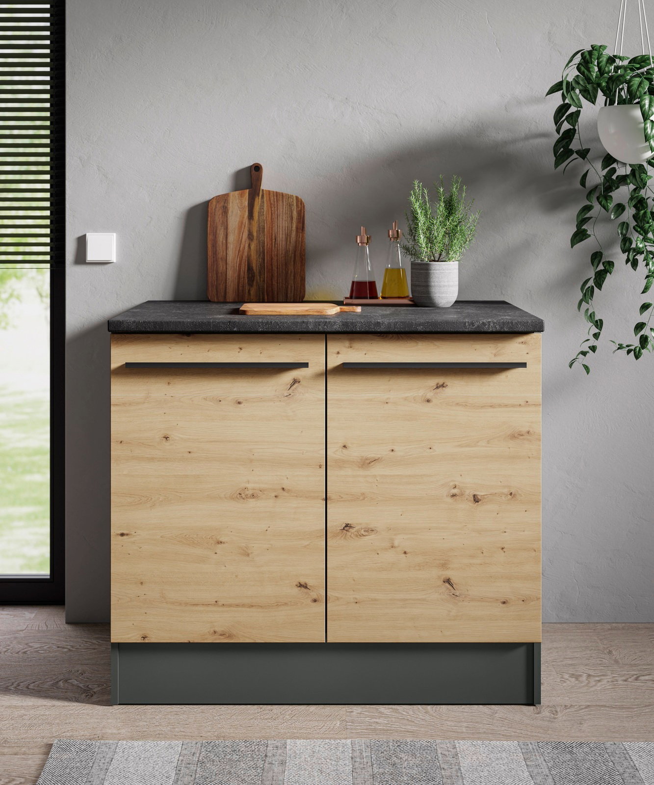 Frontansicht eines modernen Spülenunterschranks aus Holz mit dunkler Arbeitsplatte, dekoriert mit Schneidebrett, Öl- und Essigflaschen sowie einem Kräutertopf.