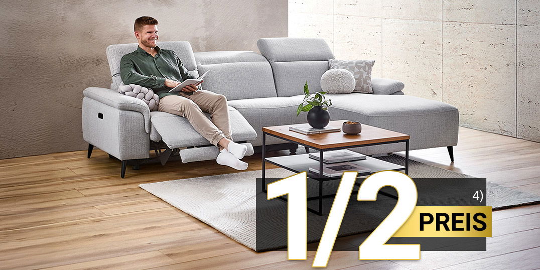 Mann entspannt auf grauem Ecksofa mit Relaxfunktion im modernen Wohnzimmer, Kaffeetisch davor, 1/2 Preis Hinweis