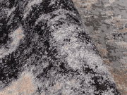 Nahaufnahme eines Designer-Teppichs mit abstraktem Muster in Grau- und Beigetönen, perspektivisch von der Seite aufgenommen.