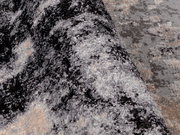 Nahaufnahme eines Designer-Teppichs mit abstraktem Muster in Grau- und Beigetönen, perspektivisch von der Seite aufgenommen.