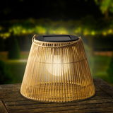 Solarbetriebene Laterne aus geflochtenem Material auf einem Holztisch, leuchtend in der Abenddämmerung, seitliche Perspektive