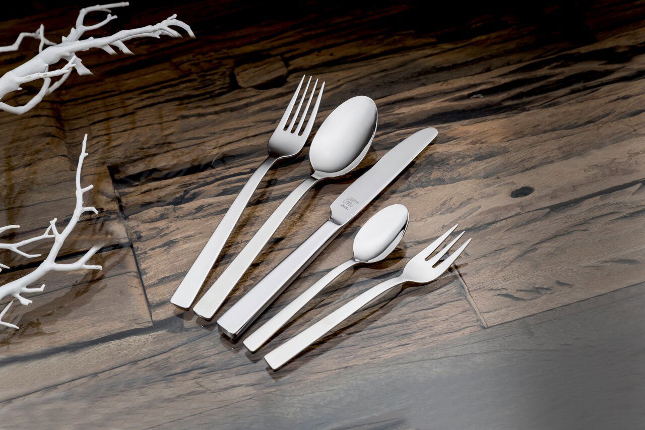 Elegantes 5-teiliges Besteckset aus Edelstahl auf einer Holzoberfläche, von oben betrachtet.