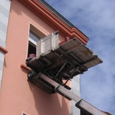Ein Sofa, das mit Hilfe eines Flaschenzuges aus dem Fenster gehievt wird, bei klarem Himmel.