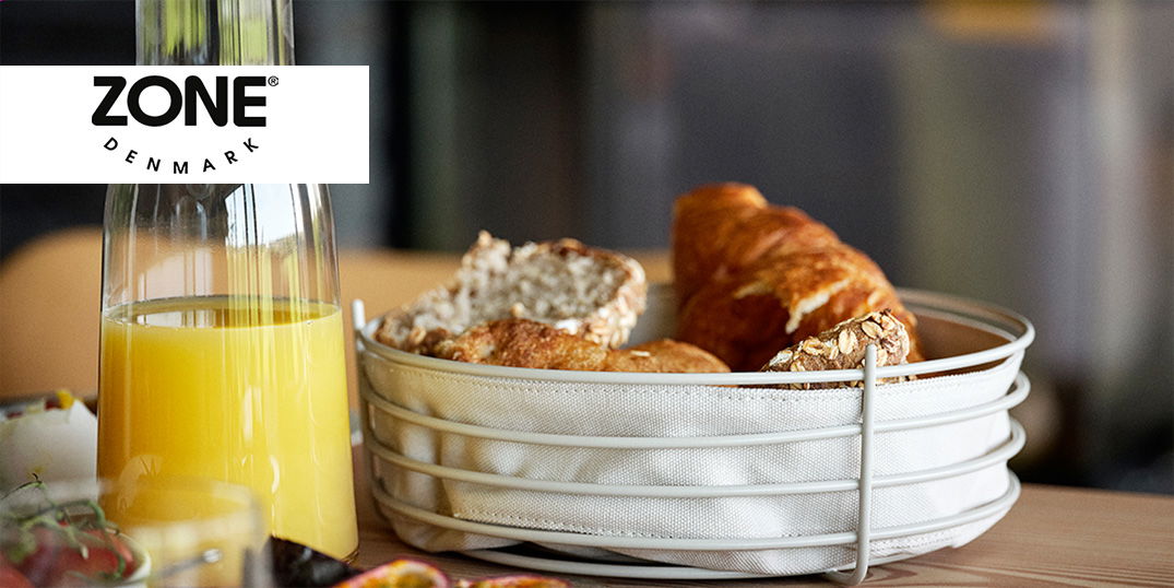 Ein Frühstückstisch mit Orangensaft in einer Flasche und einem Brotkorb mit verschiedenen Brötchen.