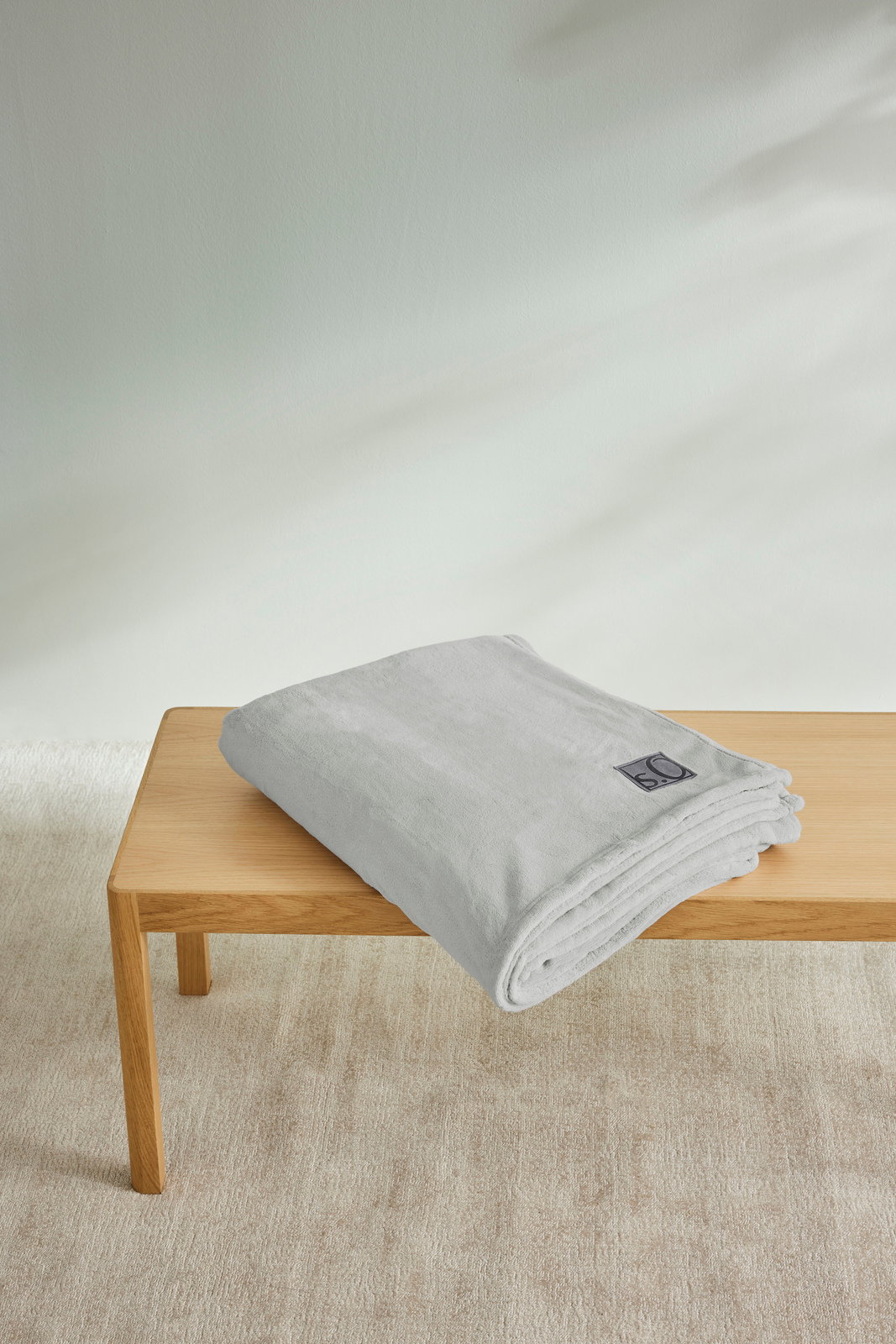 Graue s.Oliver Kuscheldecke, gefaltet auf einem Holztisch, aus seitlicher Perspektive fotografiert.