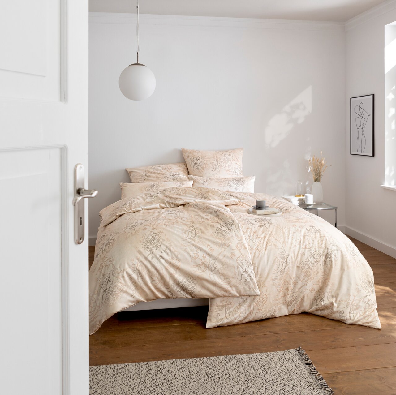 Elegante Bettwäsche in Cremefarben mit floralem Muster, auf einem Bett in einem hellen, modernen Schlafzimmer, seitliche Perspektive.