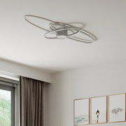 Moderne LED-Deckenleuchte mit drei überlappenden, ovalen Ringen in gebürsteter Metalloptik an weißer Zimmerdecke, fotografiert aus Untersicht (Blick nach oben) in einem hellen Wohnraum.