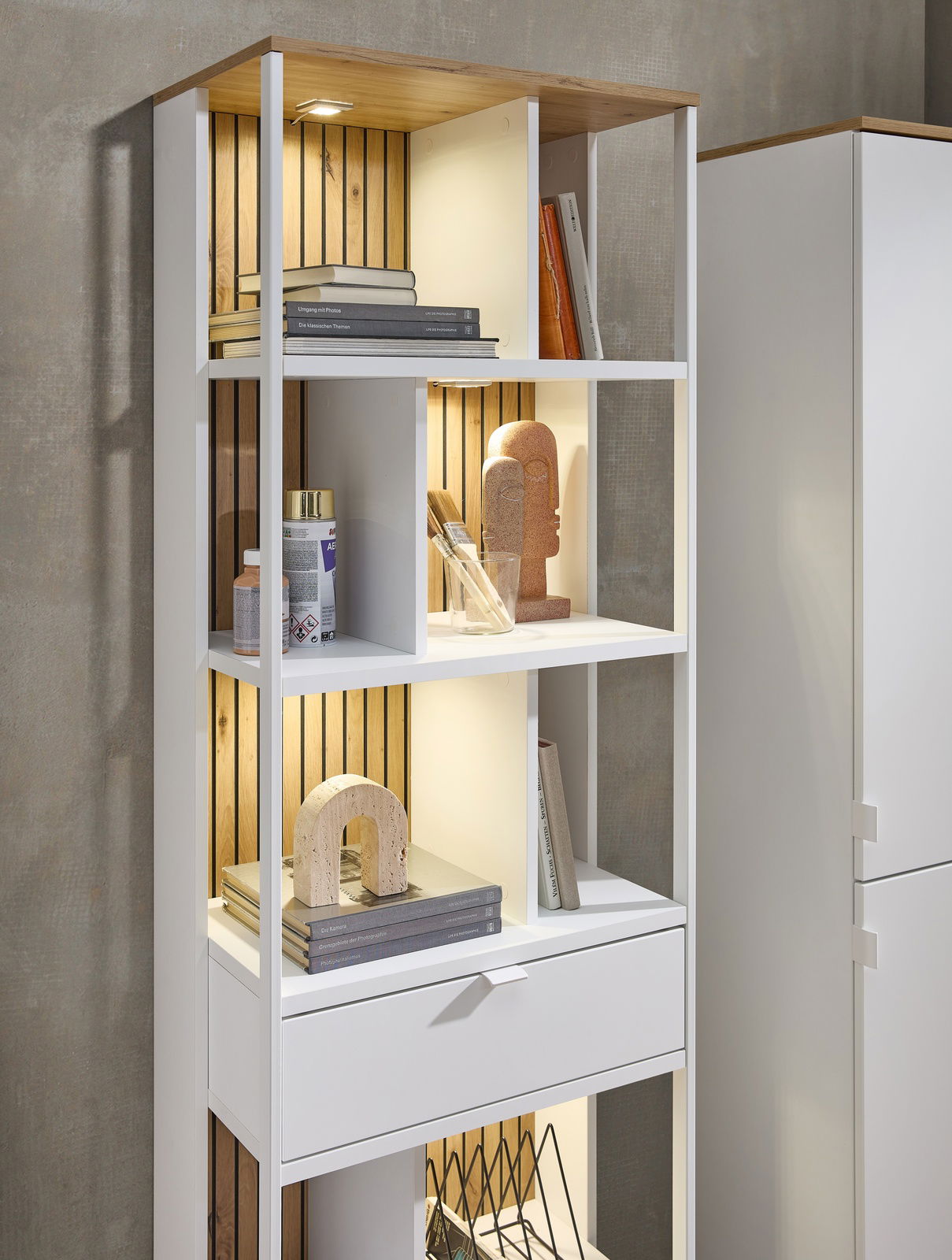 Weißes Büroregal mit mehreren Fächern, dekoriert mit Büchern und Kunstobjekten, aus seitlicher Perspektive fotografiert.